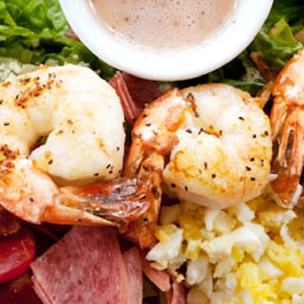 Close-up of a vibrant salad with grilled shrimp, bacon, tomatoes, and crumbled cheese.