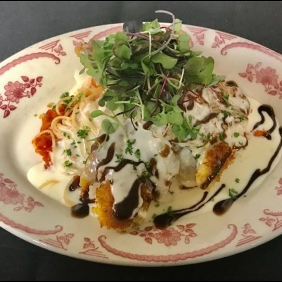 Crispy fried chicken cutlet topped with creamy sauce, balsamic glaze, pasta, and microgreens on a decorative plate.