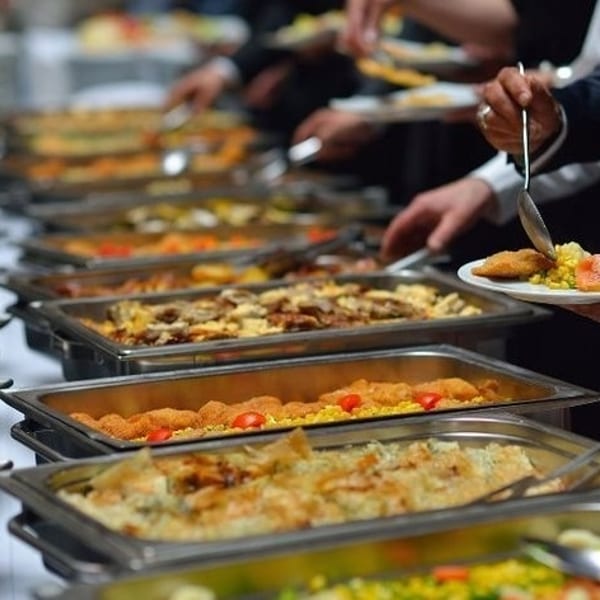 People serving themselves from a buffet line with various hot dishes in chafing dishes.